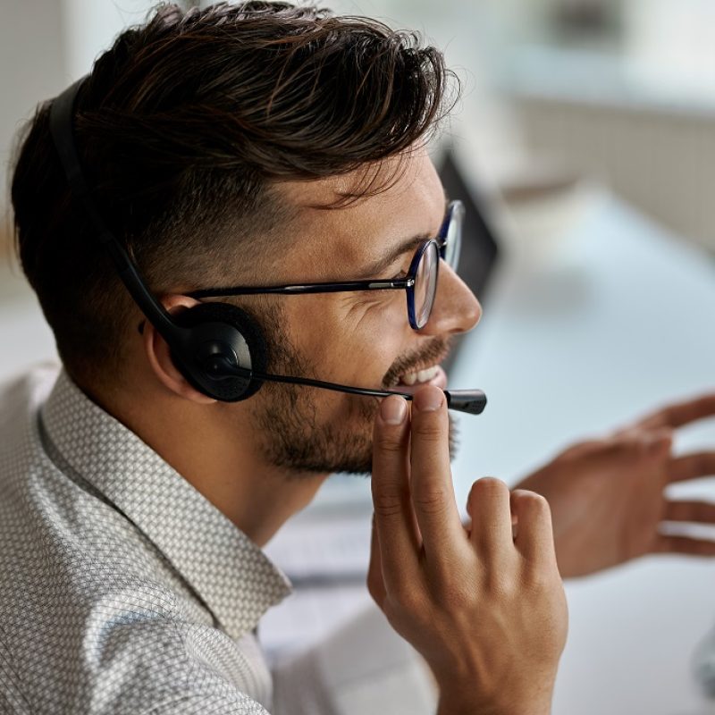 Happy call center agent wearing headset while talking with clients and working in the office.